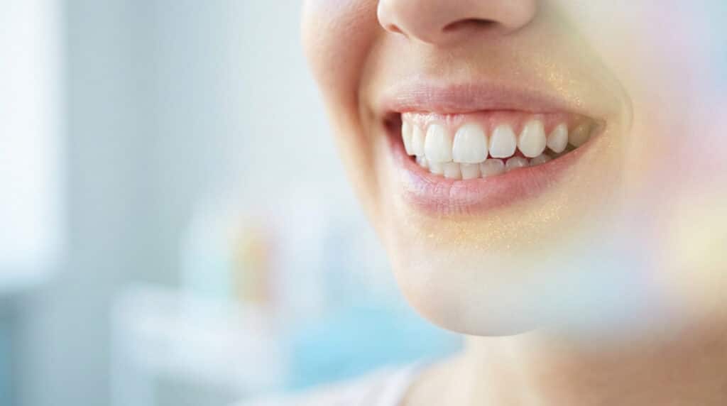 Gros plan sur le bas du visage d'une femme souriante montrant des dents blanches et saines.